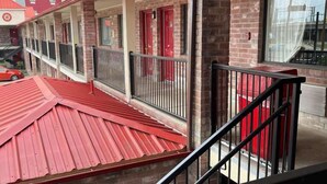 A multi-story building with a red roof, brick walls, and a balcony with a metal railing. - FairBridge Inn near Riverwalk - Alamo (San Antonio)