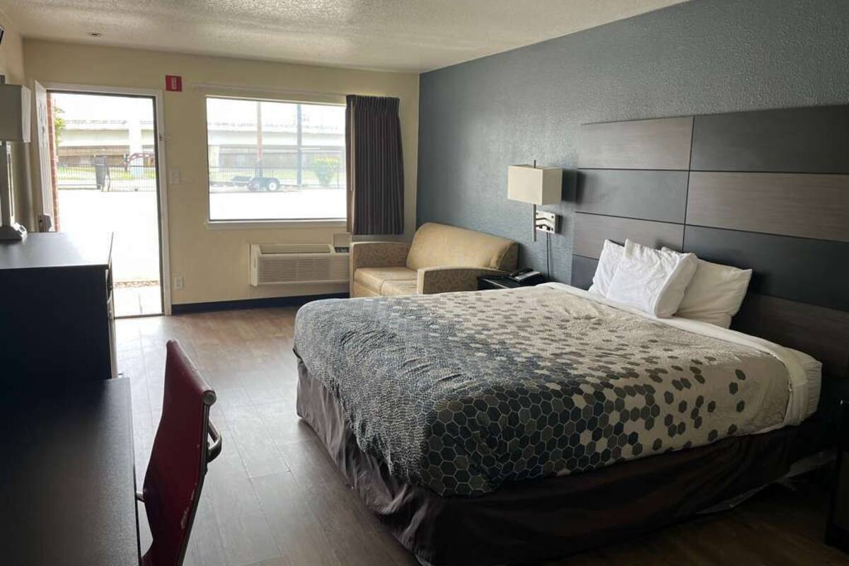 A hotel room with a bed, a desk, a chair, a window, and a door.