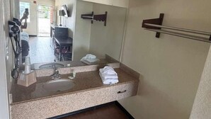 A bathroom with a sink, mirror, towel rack, and a trash bin. - FairBridge Inn near Riverwalk - Alamo (San Antonio)
