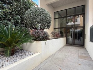 Ein moderner Hauseingang mit Glastür, ein gepflegter Garten mit verschiedenen Sträuchern und einem Betonweg.