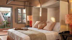 A bedroom with a bed, bedside tables, a tray of fruits and glasses, a window with curtains, and a view of a staircase and greenery outside. - Terra Verde Oia Suites - Ember Deluxe Room (Oia)