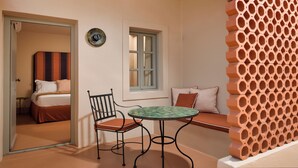 A room with a bed, a chair, a table, a window, and a decorative wall. - Terra Verde Oia Suites - Ember Deluxe Room (Oia)
