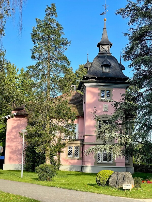 Un edificio rosa con una torre, rodeado de árboles y un cielo despejado.