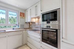 Una cocina moderna con armarios blancos, un horno Bosch y una ventana con vista a árboles.