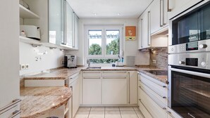 Une cuisine moderne avec des meubles blancs, un four Bosch, une fenêtre offrant une belle vue et un plan de travail sur lequel se trouve une machine à café.