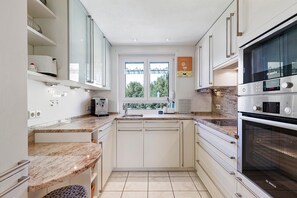 Une cuisine moderne avec des meubles blancs, un four Bosch, une fenêtre offrant une belle vue et un plan de travail sur lequel se trouve une machine à café.