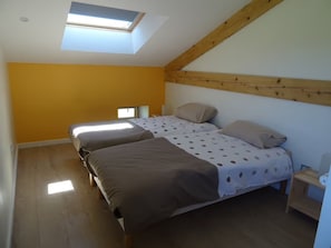 A bedroom with two beds, a skylight, wooden beams, and a small window.