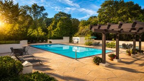 Ein Swimmingpool mit Liegestühlen und einer Pergola, umgeben von viel Grün.