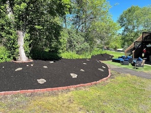 Un jardín ajardinado con un parterre circular de mantillo, una terraza de madera y mobiliario de exterior.