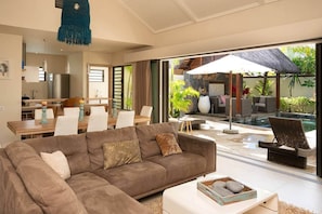Ein modernes Wohnzimmer mit einer Couch, einem Essbereich und Blick auf einen Poolbereich im Freien.