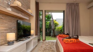 Ein modernes Hotelzimmer mit Flachbildfernseher, einer roten Bettdecke und Blick auf einen tropischen Garten.