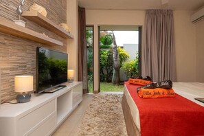 Ein modernes Hotelzimmer mit Flachbildfernseher, einer roten Bettdecke und Blick auf einen tropischen Garten.