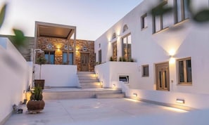 A modern building with a stone facade, a staircase leading to an upper level, and exterior lighting. - Joyful (Tinos)