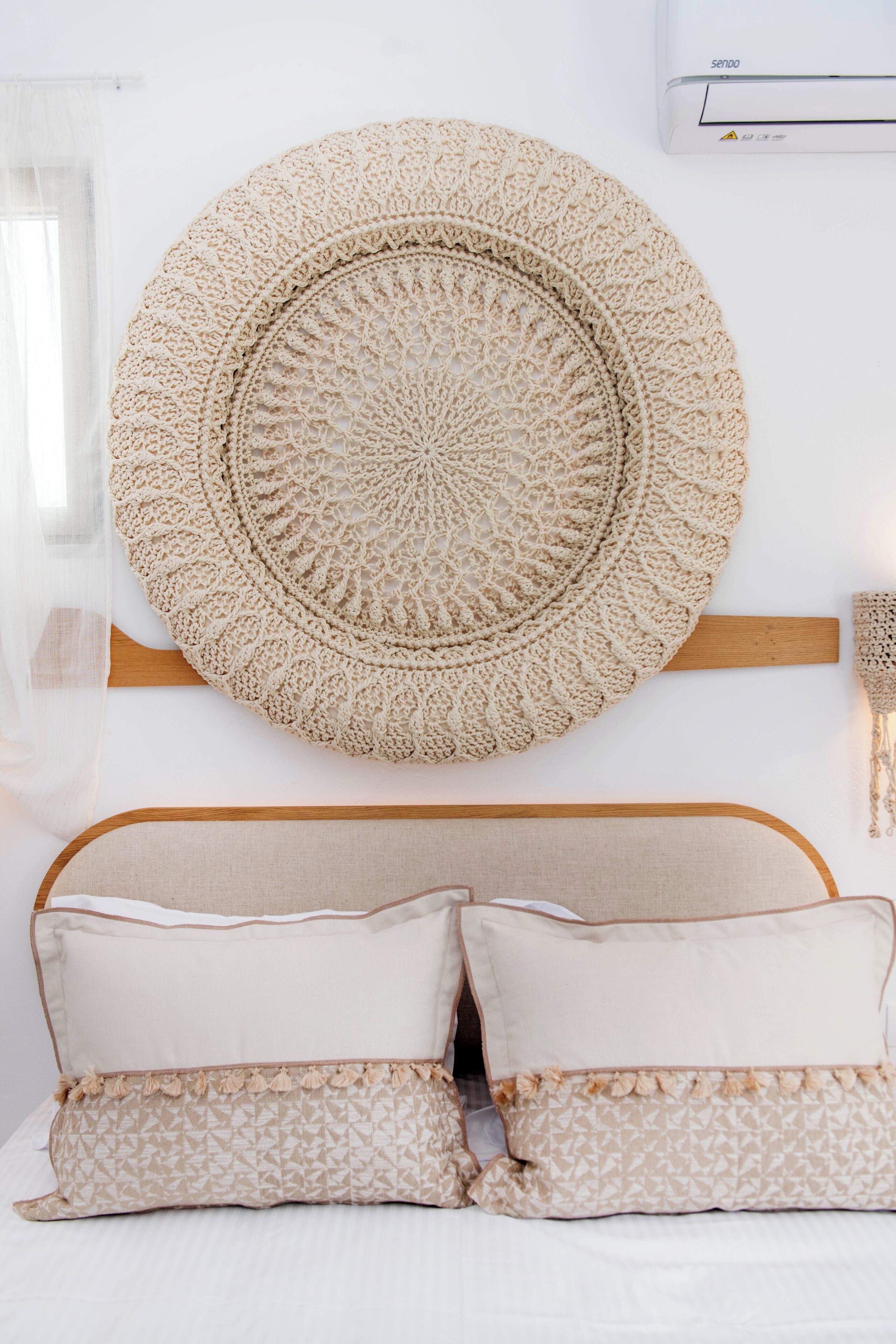 Una cama con cabecera de madera, un tapiz circular grande y un aire acondicionado fijado a la pared.