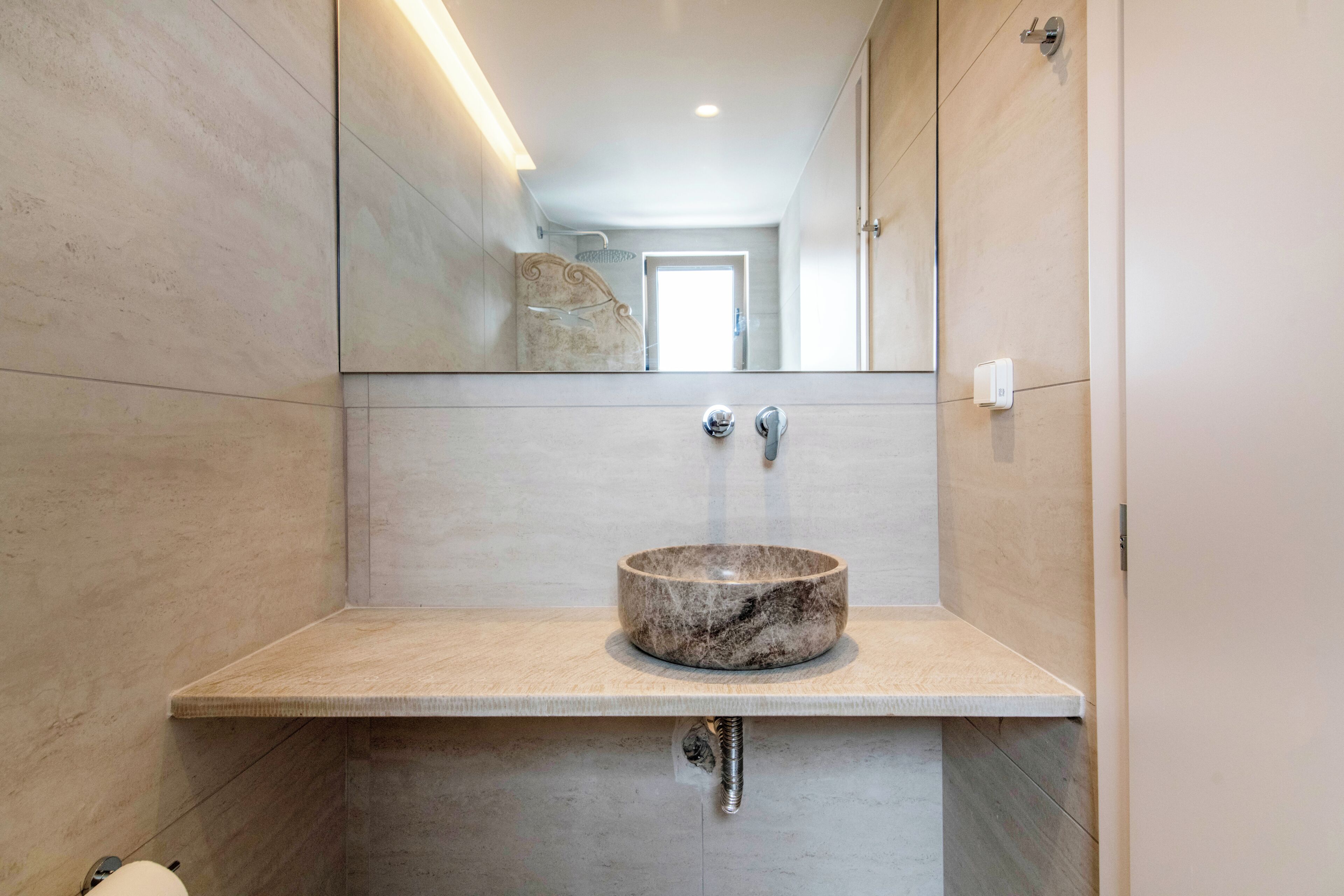 Une salle de bain avec un lavabo en marbre, un miroir et un luminaire.