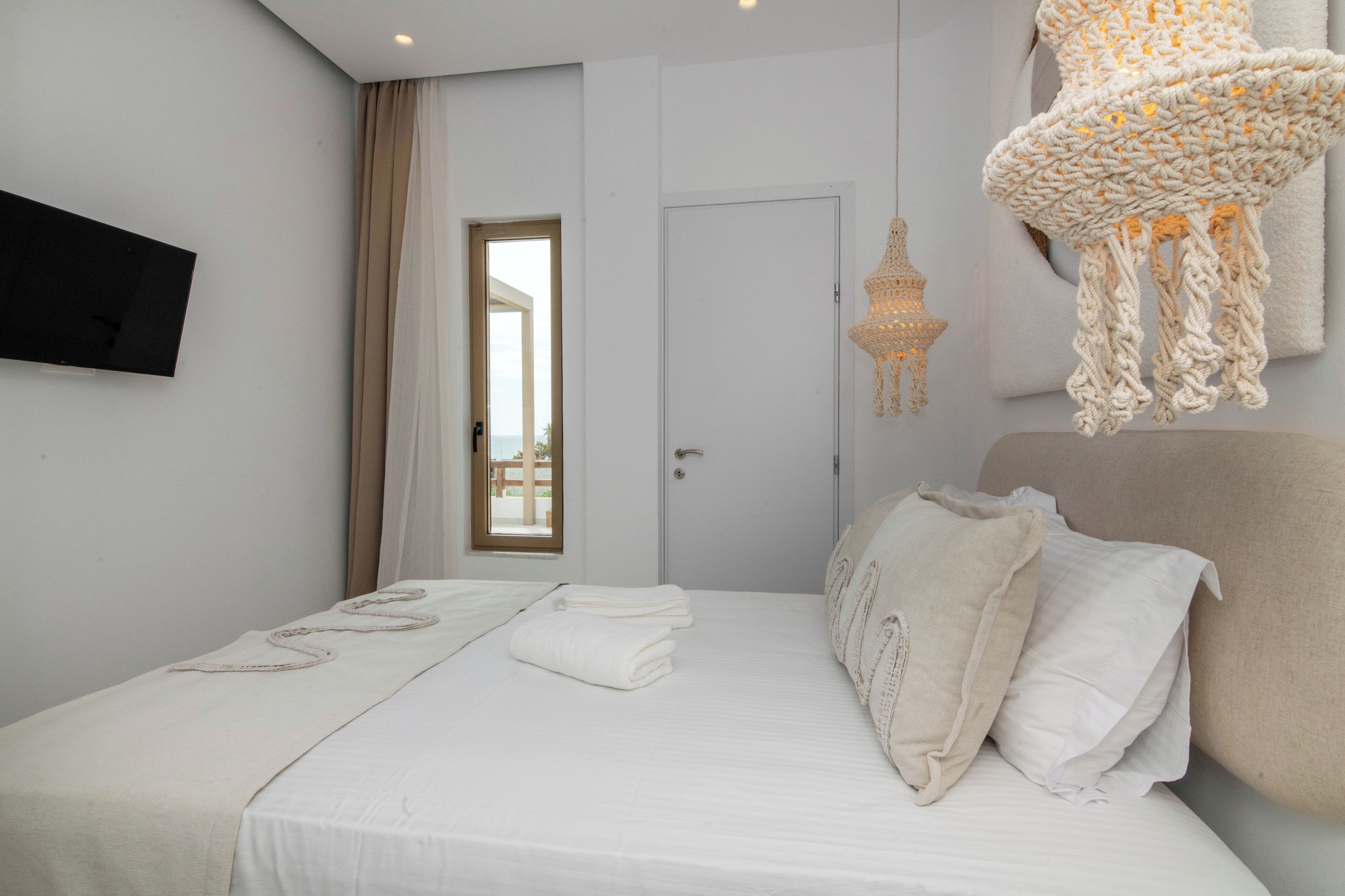 Een slaapkamer met een bed, een televisie, een deur en een hangende lamp.
