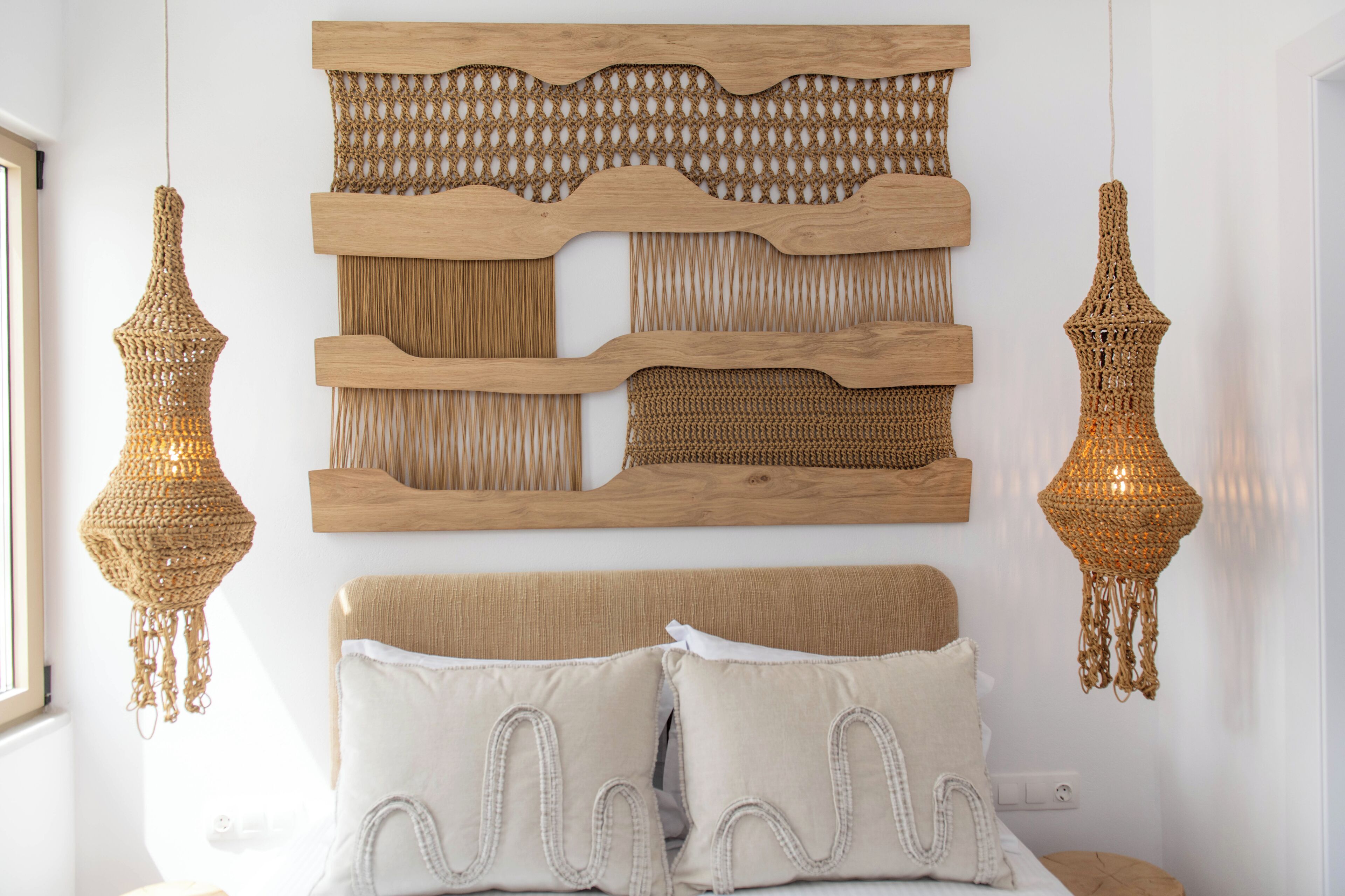 A bed with two pillows, a woven headboard, and two hanging lamps.