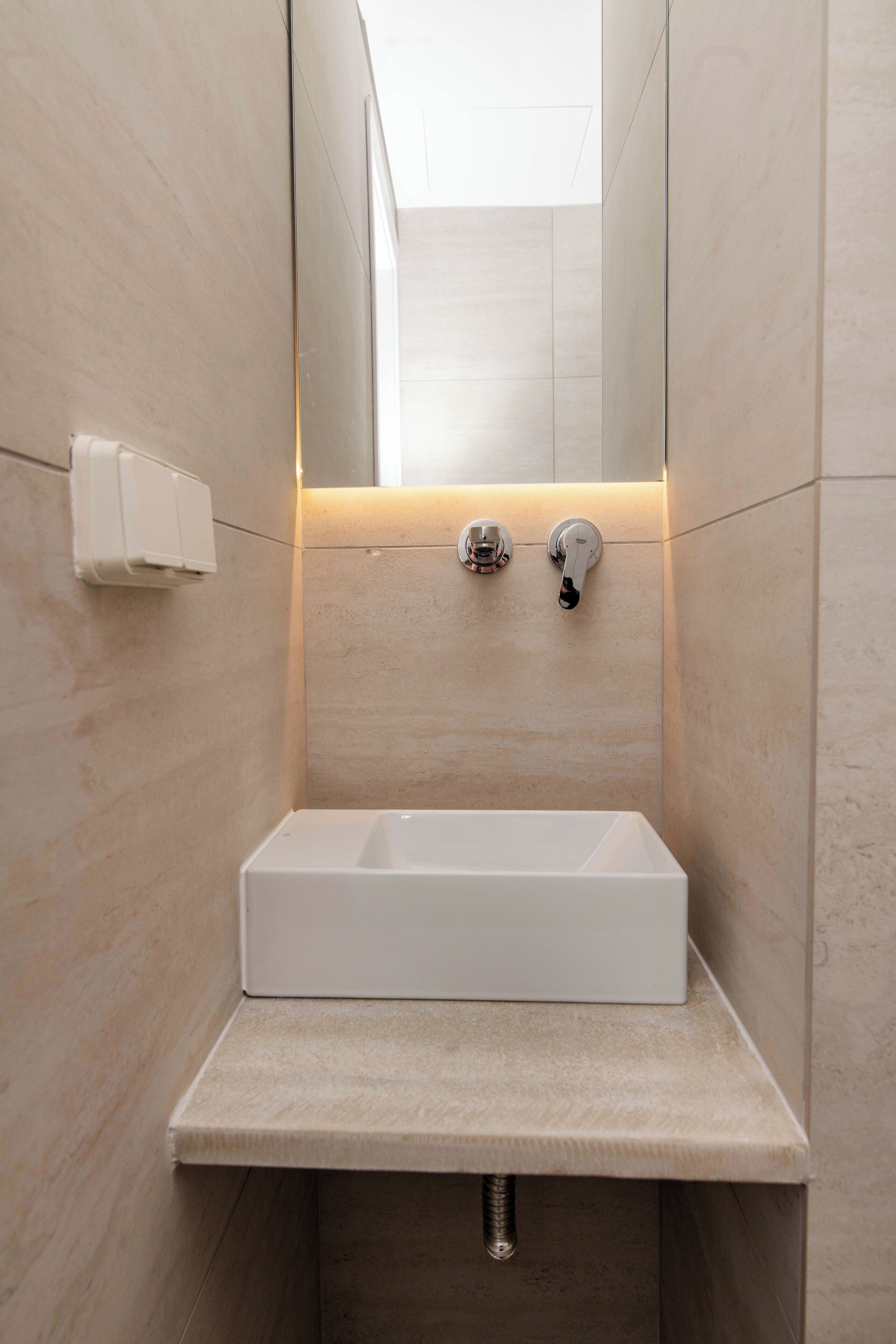 A modern bathroom with a rectangular sink, a mirror, and a light fixture above the mirror.
