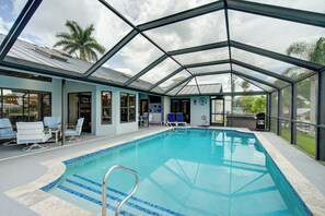 Una piscina techada con techo de cristal, sillas de descanso cercanas y vistas a palmeras.