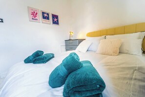 A bed with teal towels, a bedside lamp, and two framed posters on the wall. - Stylish 2bdr 10m to City Centre Free Parking (Manchester)