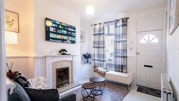 Una sala de estar con chimenea, televisor montado, un banco y una puerta.