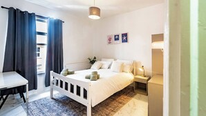 Un dormitorio con cama, mesita de noche, lámpara y vistas al exterior.