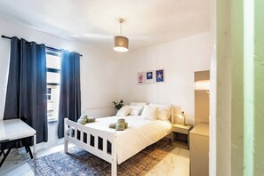 A bedroom with a bed, bedside table, lamp, and a view of the outside. - Stylish 2bdr 10m to City Centre Free Parking (Manchester)