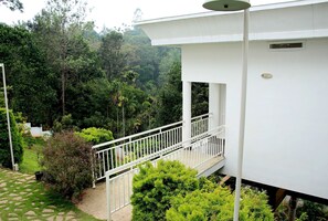 A white building with a balcony, surrounded by lush greenery and a stone pathway. - THE FOG Munnar Resorts AND SPA (Devikolam)