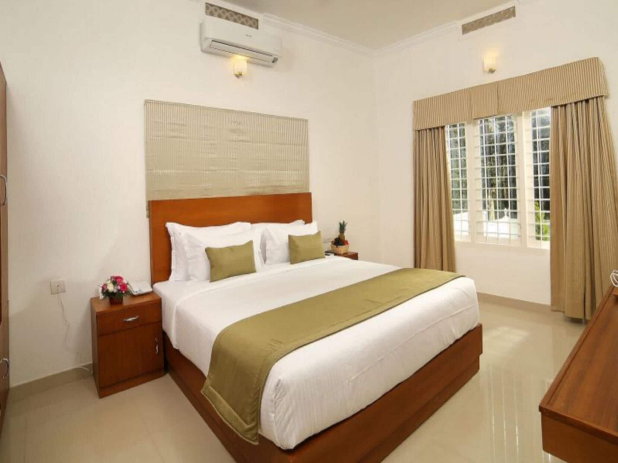 A hotel room with a large bed, a nightstand, a wooden dresser, and a window with curtains.