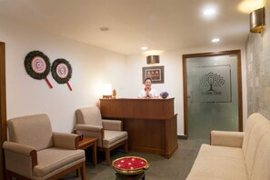 A reception area with a wooden desk, two chairs, a Buddha statue, and a Bodhi Tree sign on the door.
