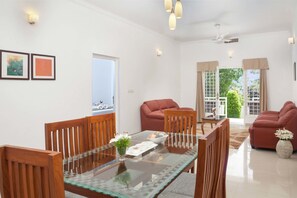 A modern living room with a glass-top dining table, wooden chairs, a red sofa, and a view of the outdoors. - THE FOG Munnar Resorts AND SPA (Devikolam)