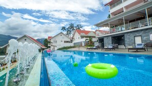 A swimming pool with lounge chairs, a water feature, and buildings in the background. - THE FOG Munnar Resorts AND SPA (Devikolam)