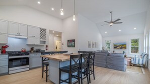 Une cuisine moderne dotée d’un îlot central, d’un coin repas avec des chaises, d’un canapé et d’un ventilateur de plafond.