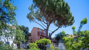 A residential building with a large tree in front, a balcony, and a clear blue sky. - Charming Holiday Apartment in the Heart of Postup Vineyards – Spectacular Sea Views! (Orebić)