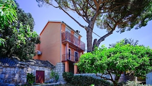 A building with a red door, a balcony, and a tree in the foreground. - Charming Holiday Apartment in the Heart of Postup Vineyards – Spectacular Sea Views! (Orebić)