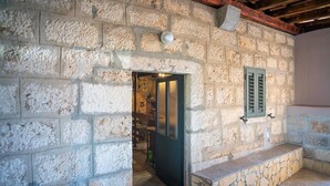 A rustic stone interior with a doorway leading to another room, a stone bench, and a window with shutters. - Charming Holiday Apartment in the Heart of Postup Vineyards – Spectacular Sea Views! (Orebić)