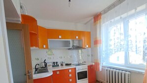 Eine Küche mit orangefarbenen Schränken, einem Herd, einer Spüle und einem Fenster mit Vorhängen.