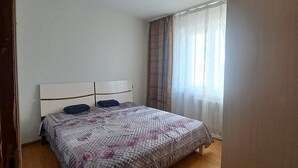 Ein Schlafzimmer mit einem Bett, Holzboden, einer Kopfstütze und einem Fenster mit Vorhängen.