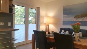 A modern living room with a dining area, a lamp, a painting, and a vase with flowers. - Enjoy Sea Views & Tranquility – Exclusive Penthouse Apartment in Lauterbach Harbor (Putbus)