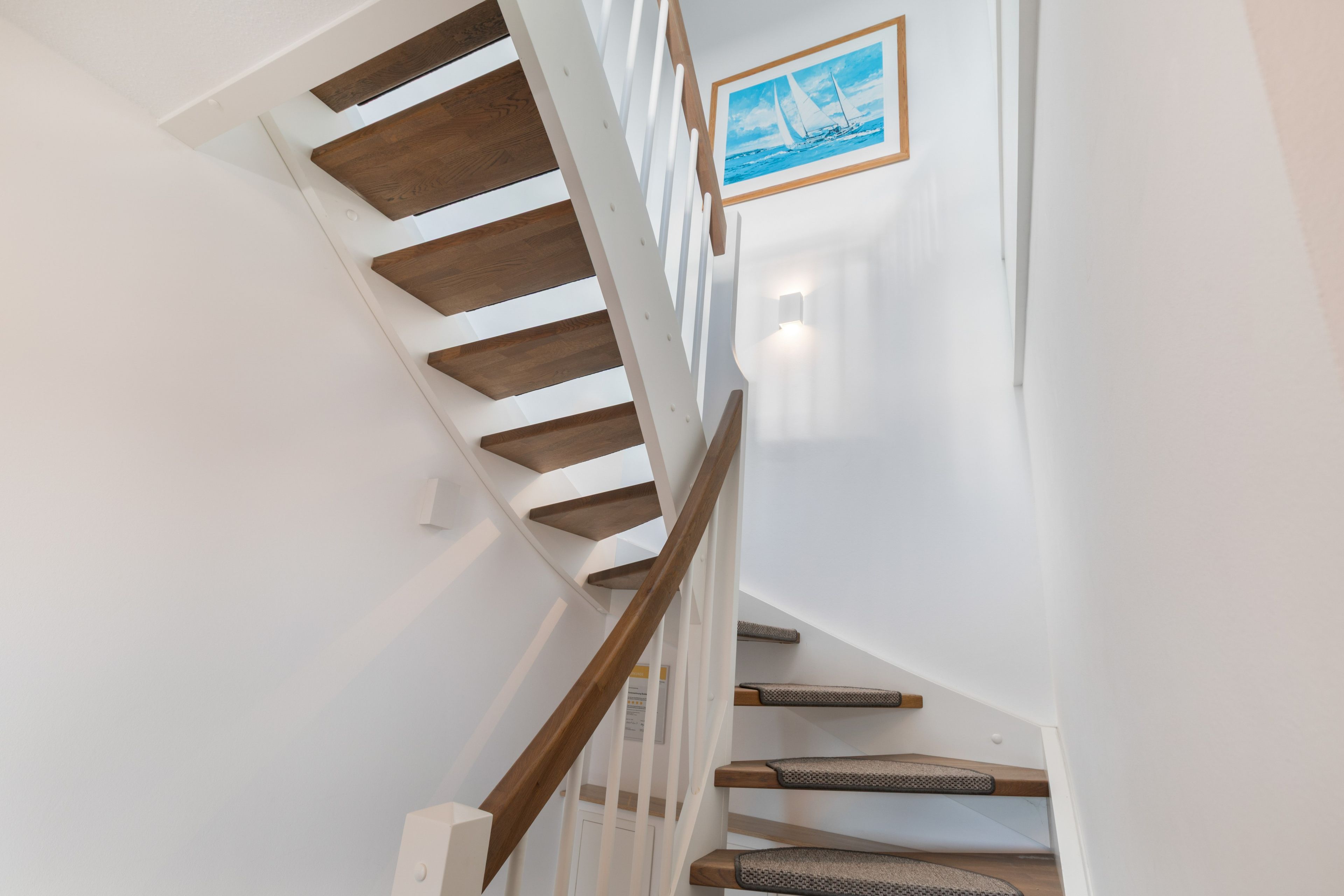 A staircase with wooden steps and white walls, leading to a landing with a framed picture.