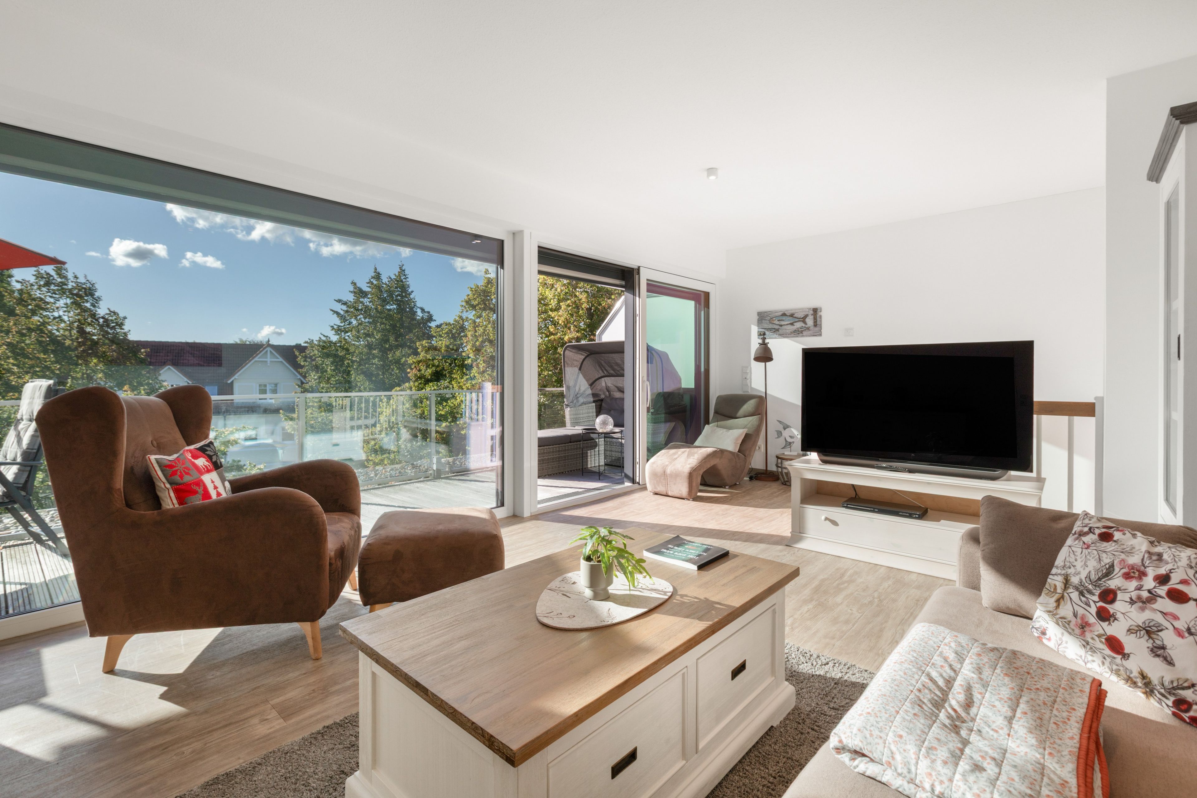 A modern living room with a flat-screen TV, comfortable seating, and a balcony with a glass door.