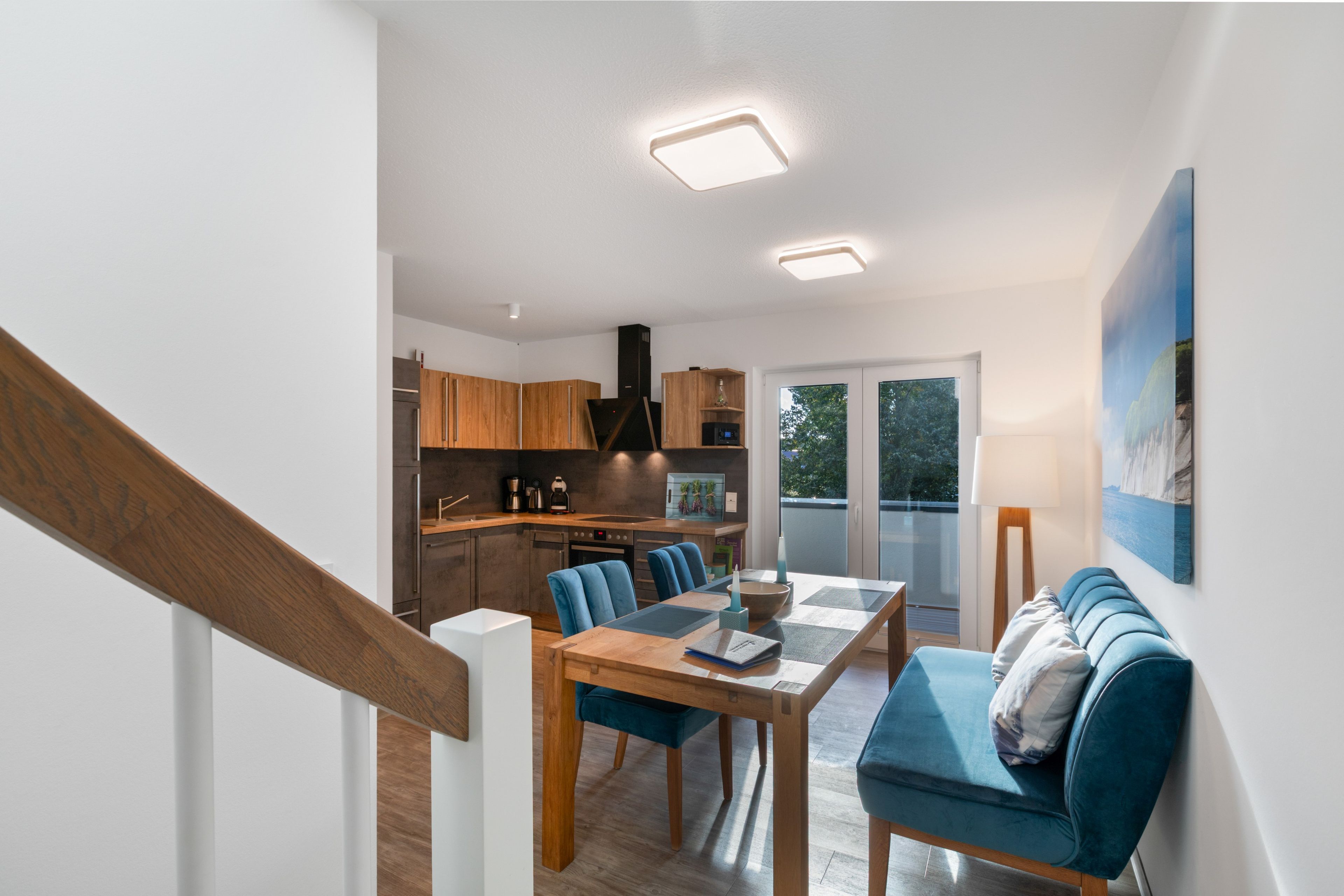 A modern kitchen with wooden cabinets, a dining table with chairs, and a view of the outdoors through a sliding glass door.