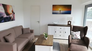 Ein modernes Wohnzimmer mit einer Couch, einem Sessel, einem Couchtisch und einem Gemälde, das einen Sonnenuntergang über dem Wasser zeigt.