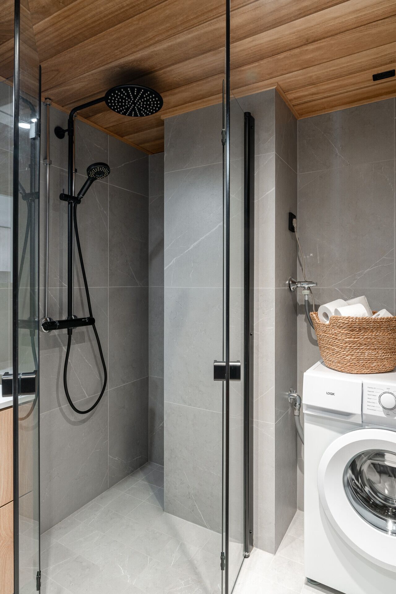 A modern bathroom with a glass-enclosed shower, a washing machine, and a wooden ceiling.
