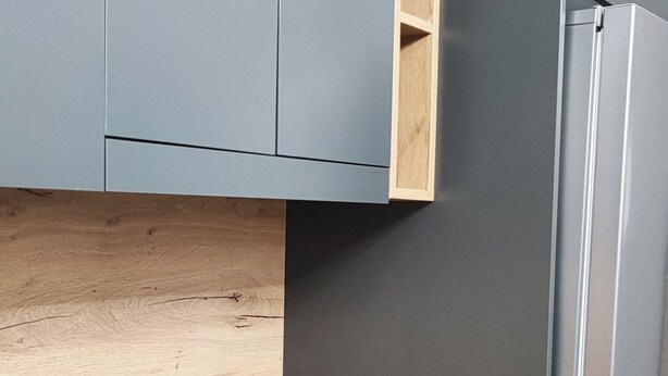 Una cocina con gabinetes grises, una placa de inducción negra y un refrigerador de acero inoxidable.