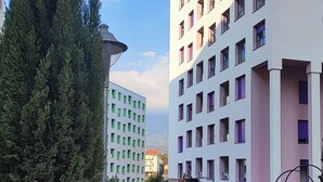 Un edificio moderno de varios pisos, un paseo pavimentado y una barandilla de metal azul.