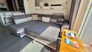 Een moderne woonkamer met een modulaire bank, een houten salontafel en een keuken in de achtergrond.