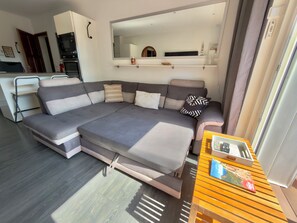 A modern living room with a sectional sofa, a wooden coffee table, and a kitchen area in the background. - In the heart of Saint-Aygulf, 300m from shops and beach (Fréjus)