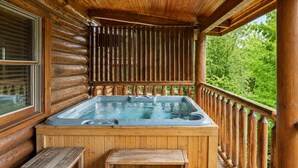 A wooden deck with a hot tub, wooden benches, and a view of greenery. - Pet-Friendly | Hot Tub | Outdoor TV | Game Room | Views | Sleeps 8 (Sevierville)