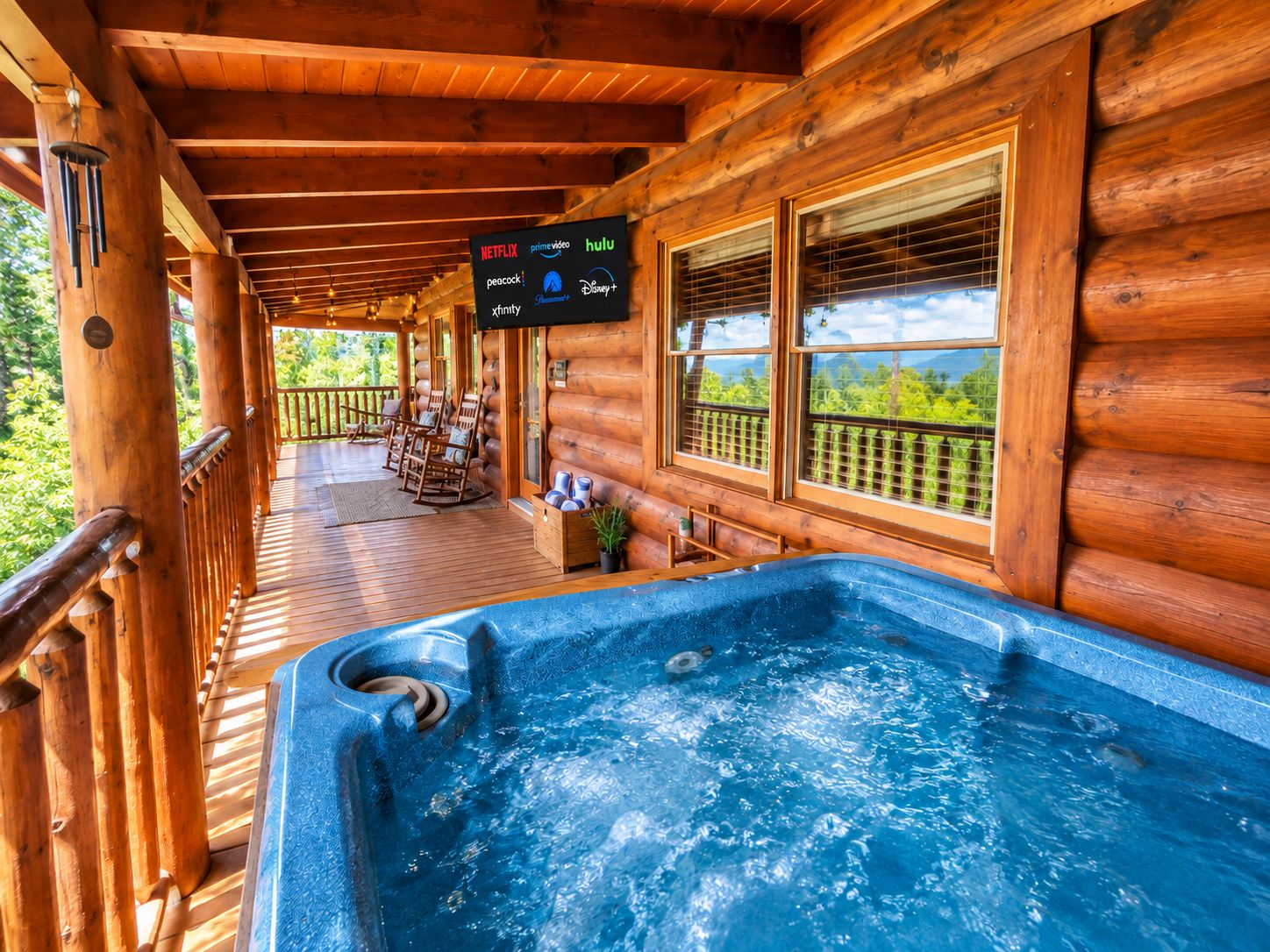 A wooden cabin with a hot tub, a covered porch with chairs, and a sign listing streaming services.